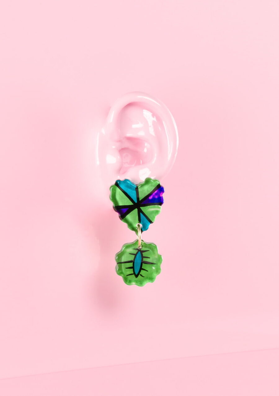 Green sustainable statement drop earrings with a hearth-shaped stud, on a pink background.