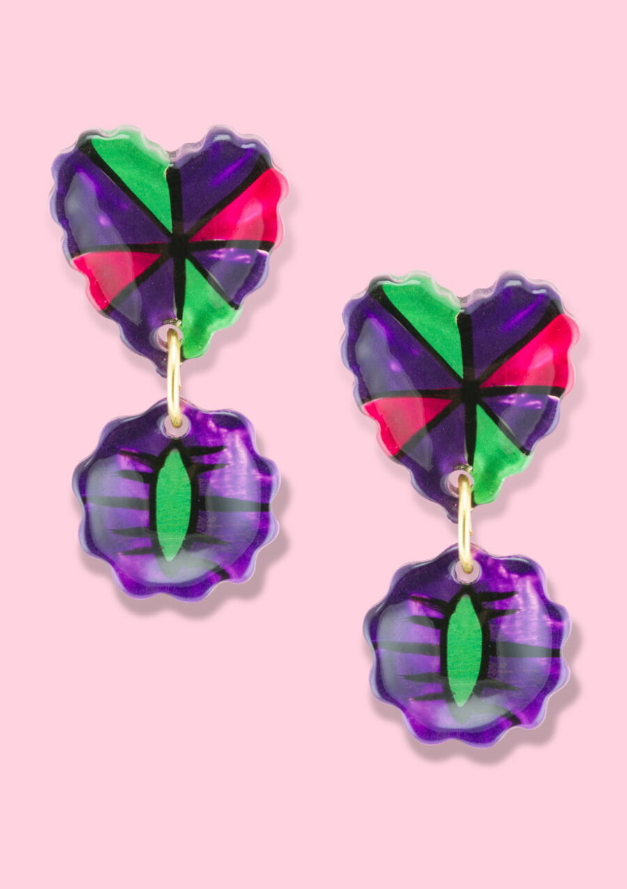 Purple drop earrings with a hearth-shaped stud, on a pink background.