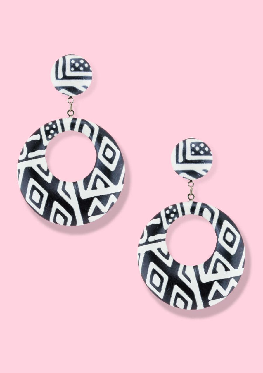 Black and white dangle earrings on a pink background.