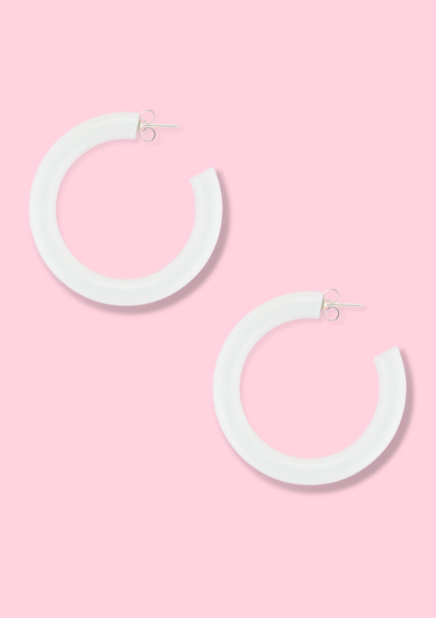 White sustainable vintage hoop earrings on a pink background.